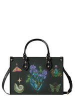 Gothic handbag with glowing blue anatomical heart and violet flowers surrounded by beetles, moths, and celestial symbols