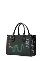 Angled view of gothic tote bag showing snake, flowers, and pink tassels design
