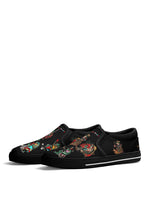Side angle of black slip-on sneakers featuring colorful tattoo frogs and bold anti-tattoo slogan on canvas