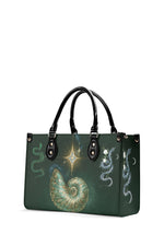 Side angle of gothic green bag showing shimmering spiral shell, star, and coiled snake with lilies