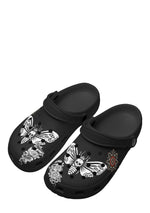 Angled view of black slip-ons featuring skull moths and floral tattoo graphics